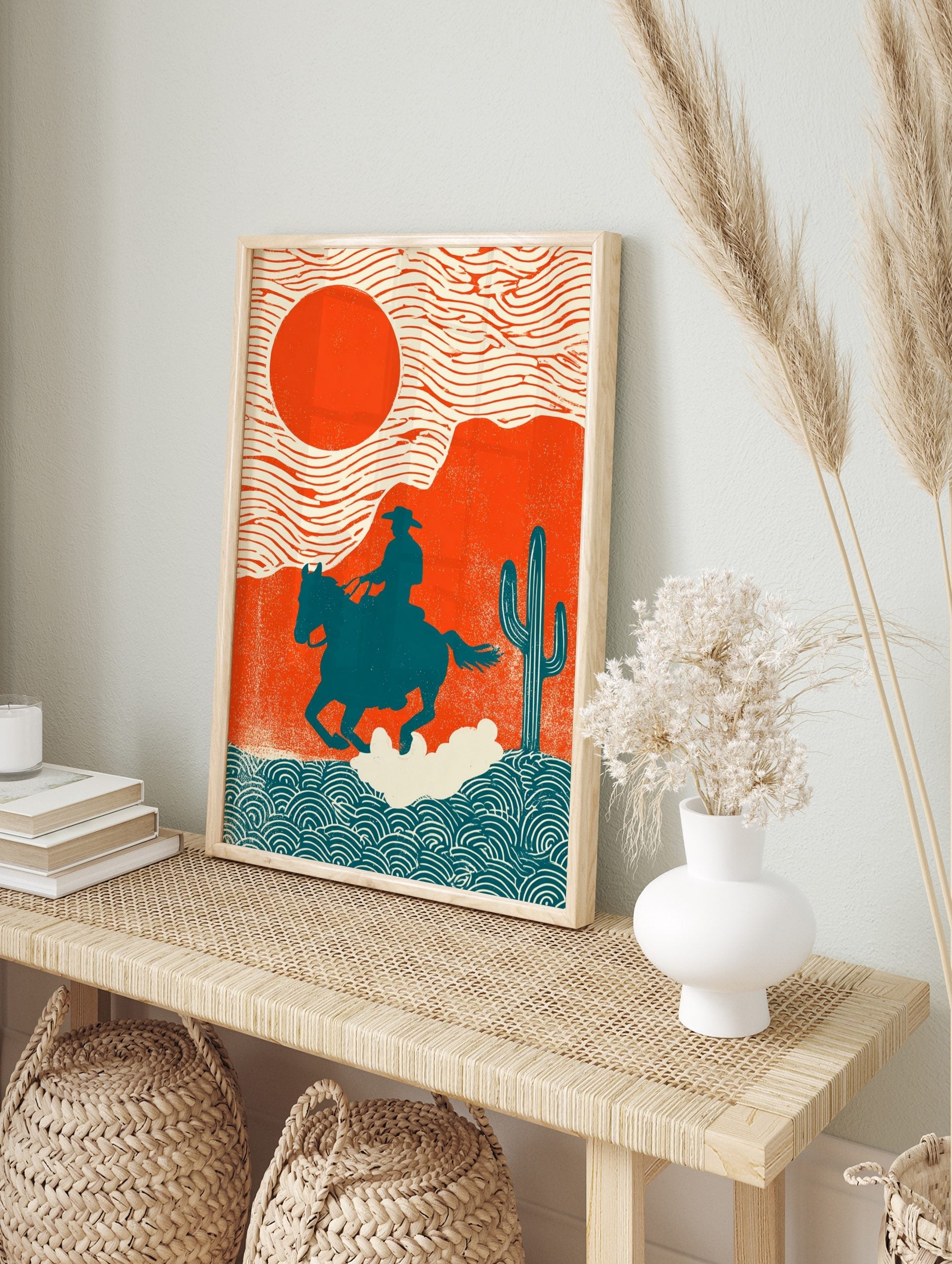 Illustrative Western art print of cowboy on horse against orange sun and desert landscape, in an alternate framed mockup