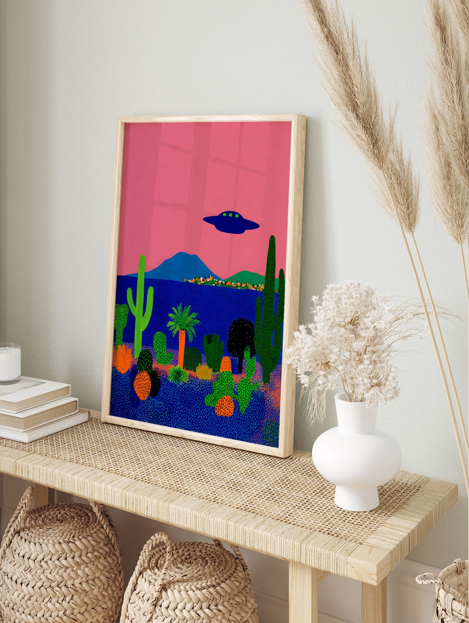 Surreal desert landscape poster with a pink sky, blue ocean, green cacti, and a dark blue UFO flying above a small town. - Image 4