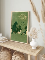 Illustration of a black dog and a white dog playing chess at a table with a tea set above, in, in an alternate framed mockup