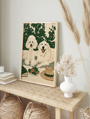 Illustrated wall art of a poodle and golden retriever on a picnic blanket with strawberries, in an alternate framed mockup