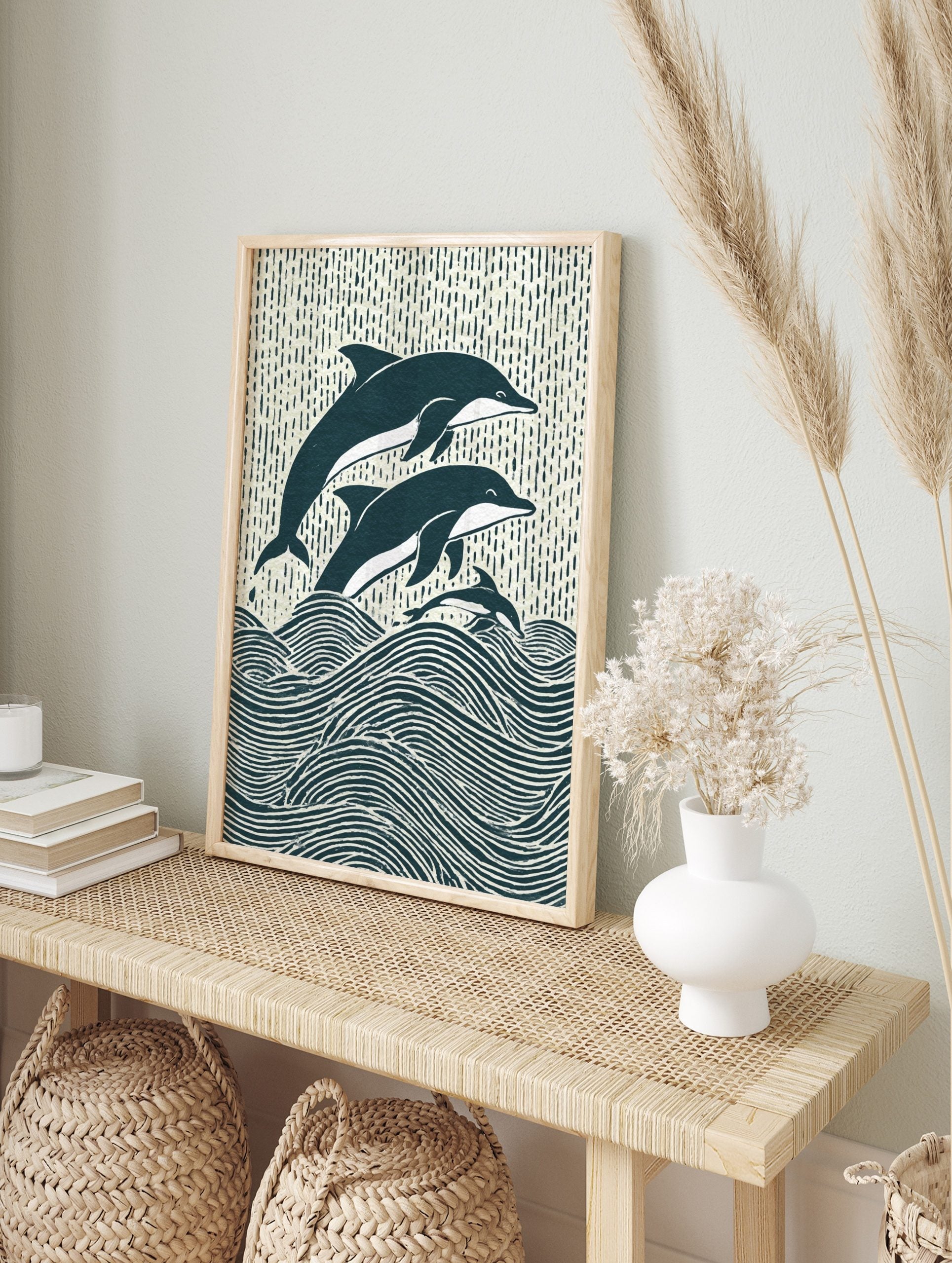 Illustrative woodcut-style print of three navy and white dolphins leaping from ocean waves, in an alternate framed mockup