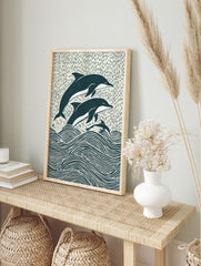 Illustrative woodcut-style print of three navy and white dolphins leaping from ocean waves, in an alternate framed mockup