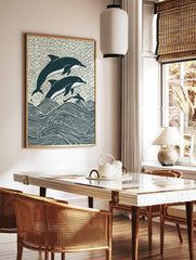 Illustrative woodcut-style print of three navy and white dolphins leaping from ocean waves, in a styled room mockup
