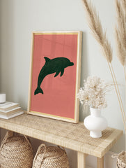 Minimalist dark green dolphin silhouette illustration on a muted pink background, unframed, in an alternate framed mockup