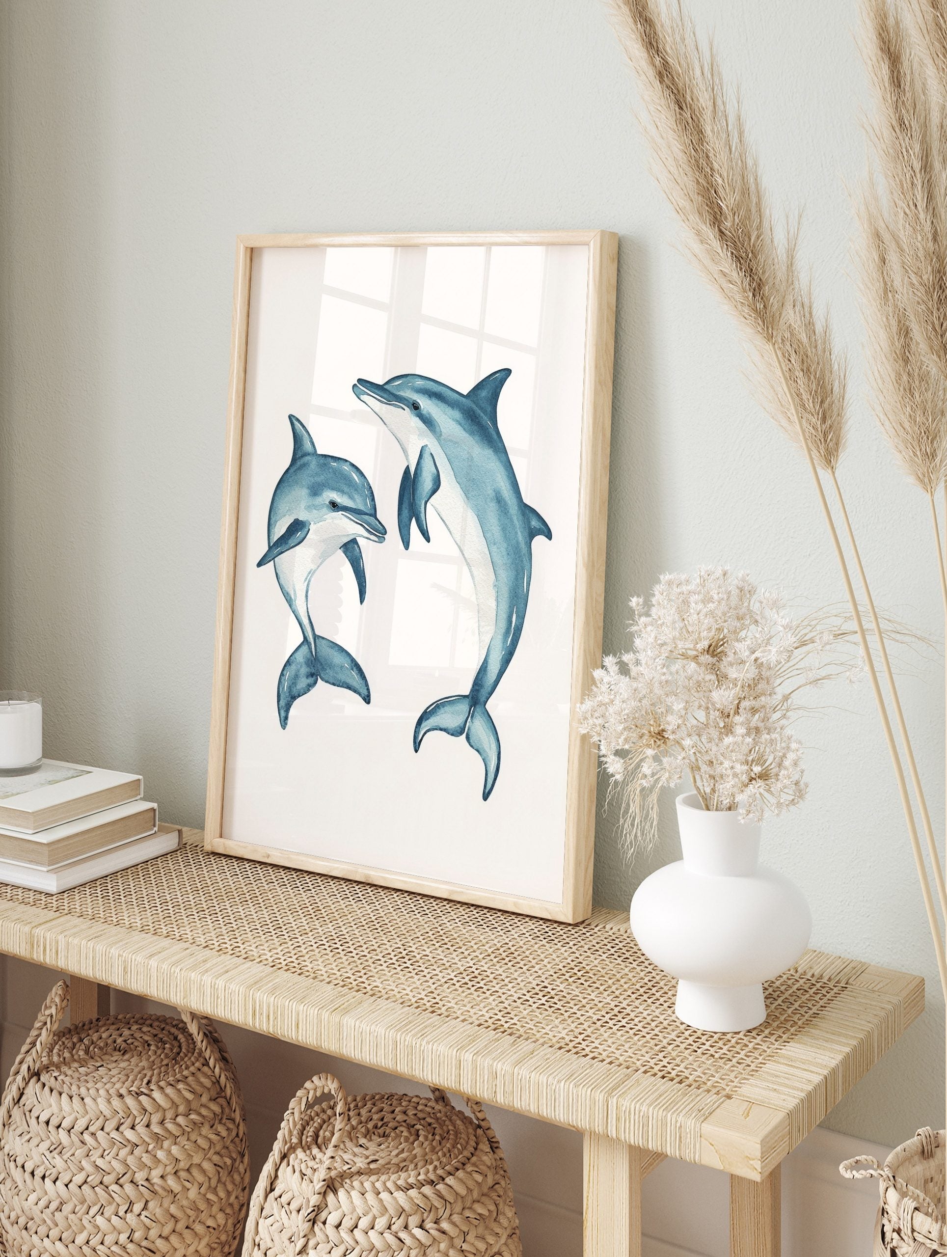 Two blue watercolour dolphins, one large and one small, in dynamic swimming poses on a white, in an alternate framed mockup