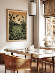 Illustrative woodcut style print of cattails, green water with ripples, and three dragonflies, in a styled room mockup