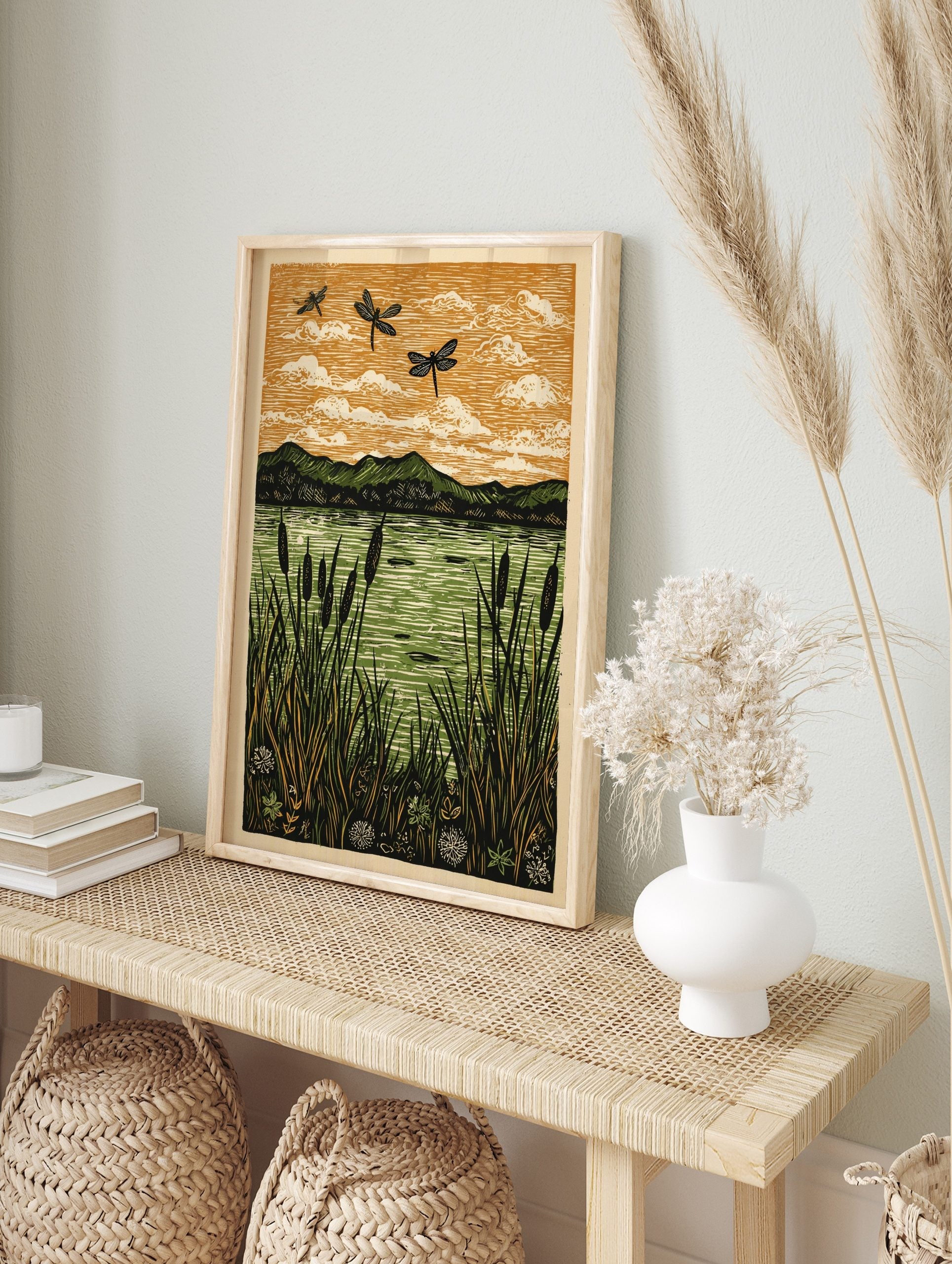 Linocut print of three black dragonflies flying over a green lake with cattails and mountains, in an alternate framed mockup