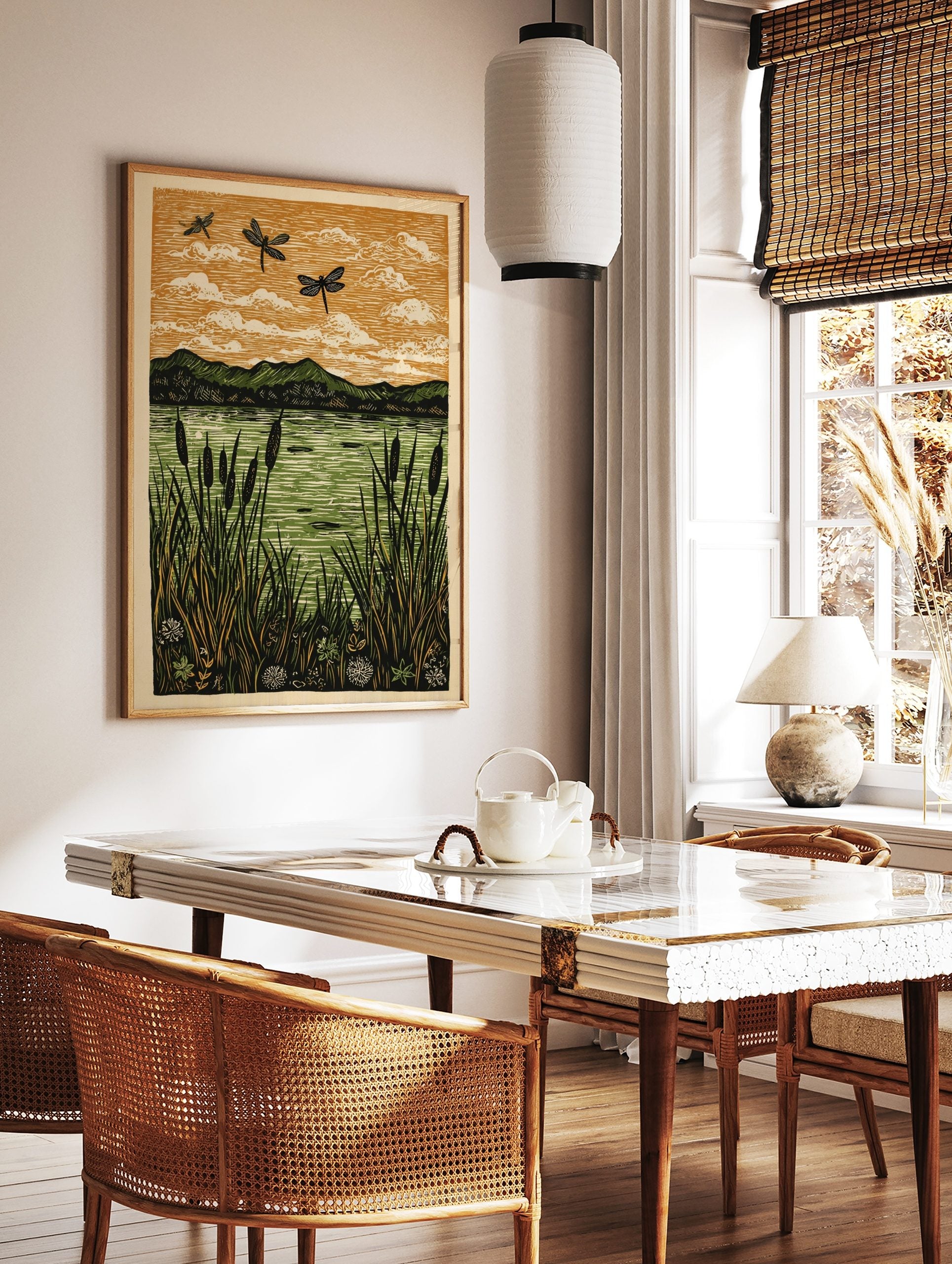 Linocut print of three black dragonflies flying over a green lake with cattails and mountains under, in a styled room mockup
