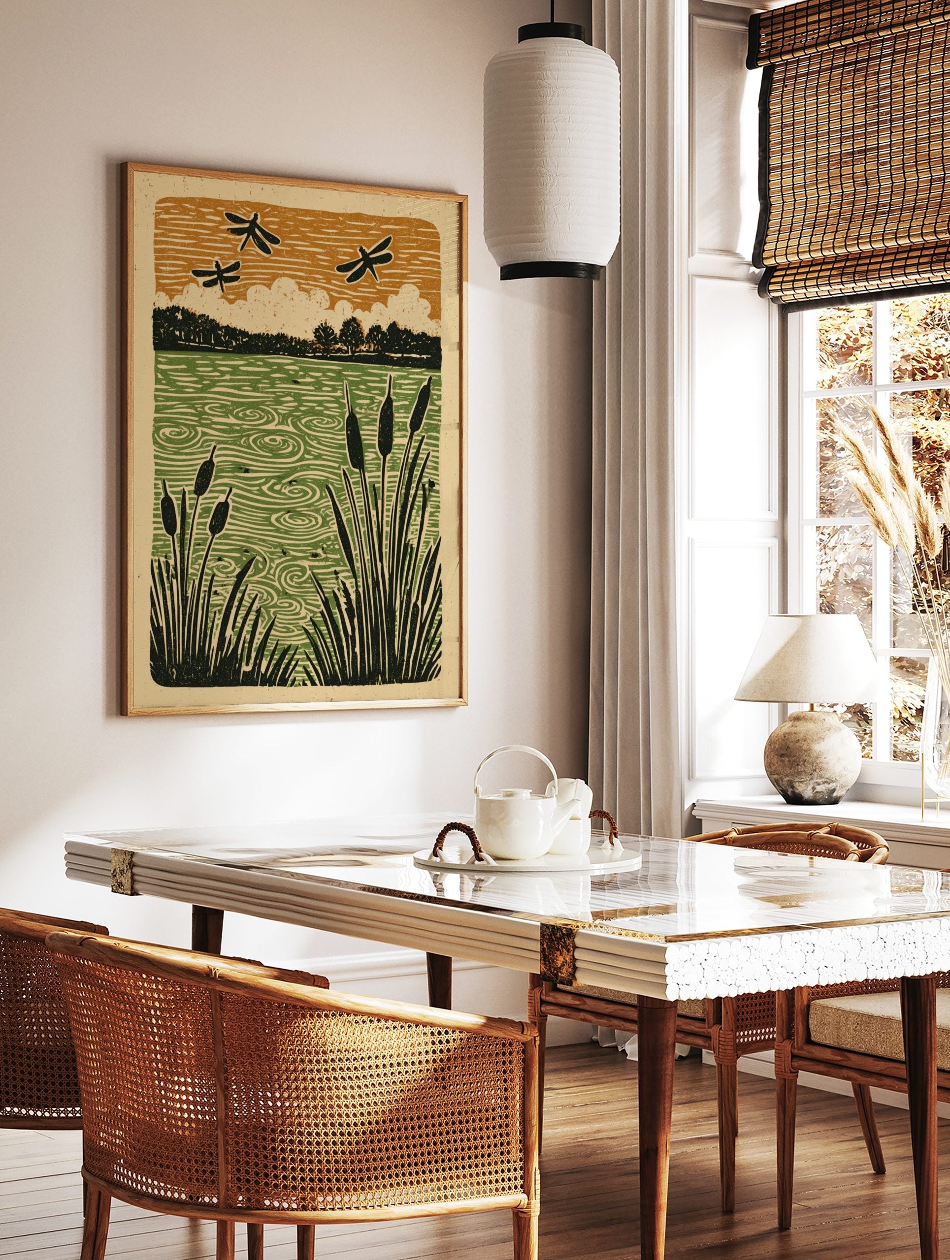 Linocut-style print of black dragonflies flying over a green pond with cattails and trees, under an, in a styled room mockup