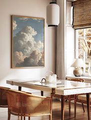 Classical painting of dramatic cumulus clouds in white, grey, and peach against a blue sky, in a styled room mockup