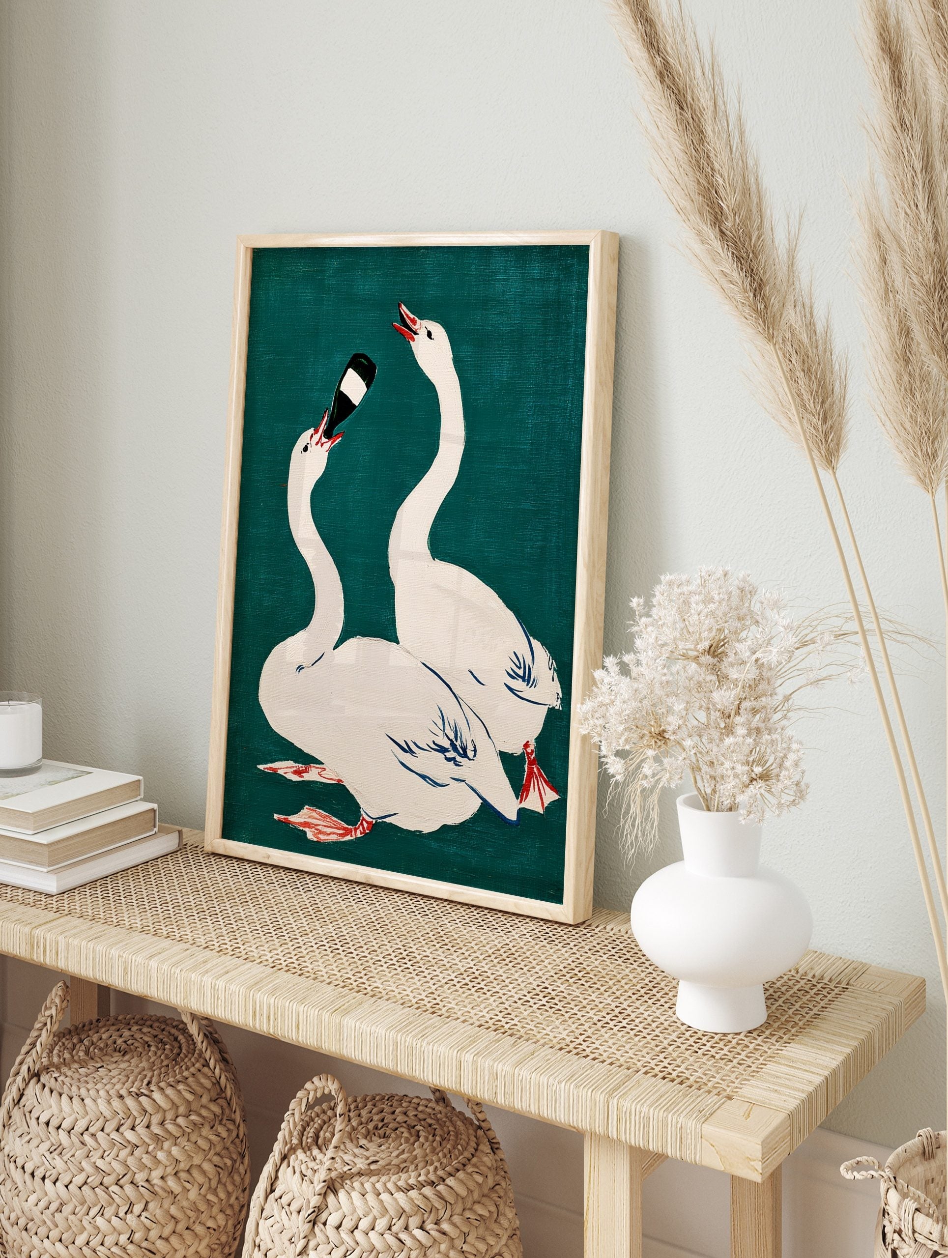 Illustrative print of two white swans on teal background, one drinking from a dark bottle, in an alternate framed mockup
