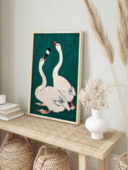 Illustrative print of two white swans on teal background, one drinking from a dark bottle, in an alternate framed mockup