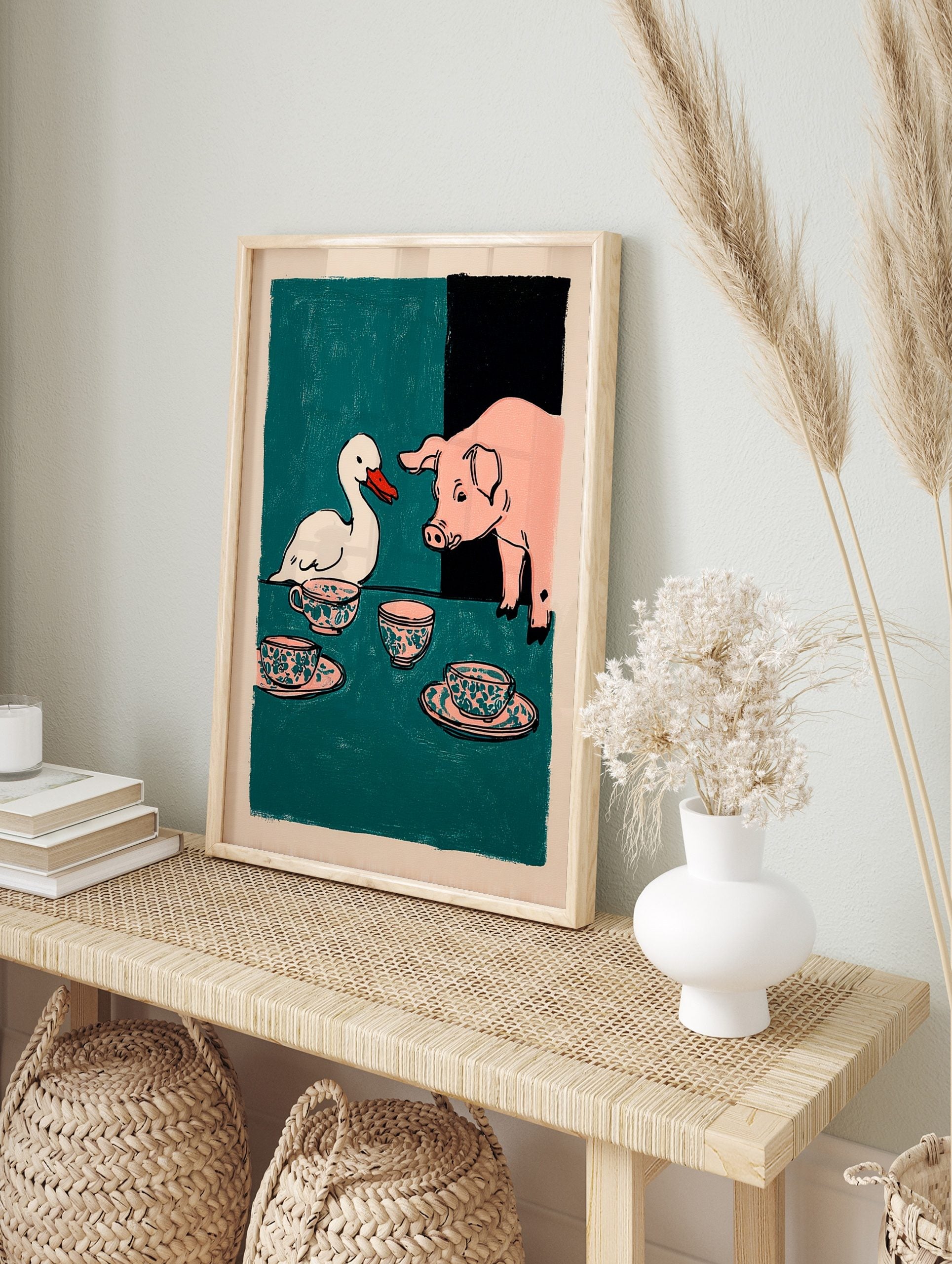 Illustrative print of a white duck and a pink pig at a tea party with patterned teacups on a, in an alternate framed mockup