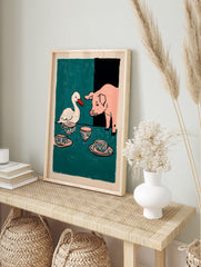 Illustrative print of a white duck and a pink pig at a tea party with patterned teacups on a, in an alternate framed mockup