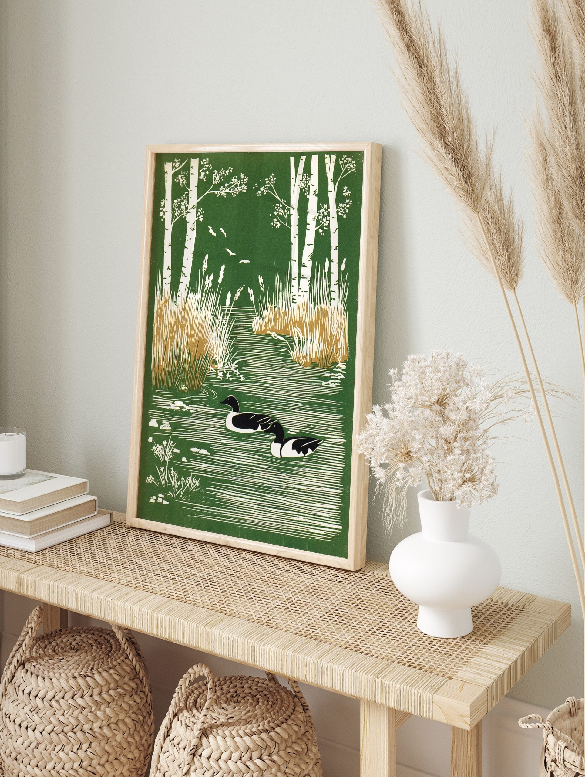 Illustrative print of two ducks swimming in a green pond framed by white birch trees and reeds, in an alternate framed mockup