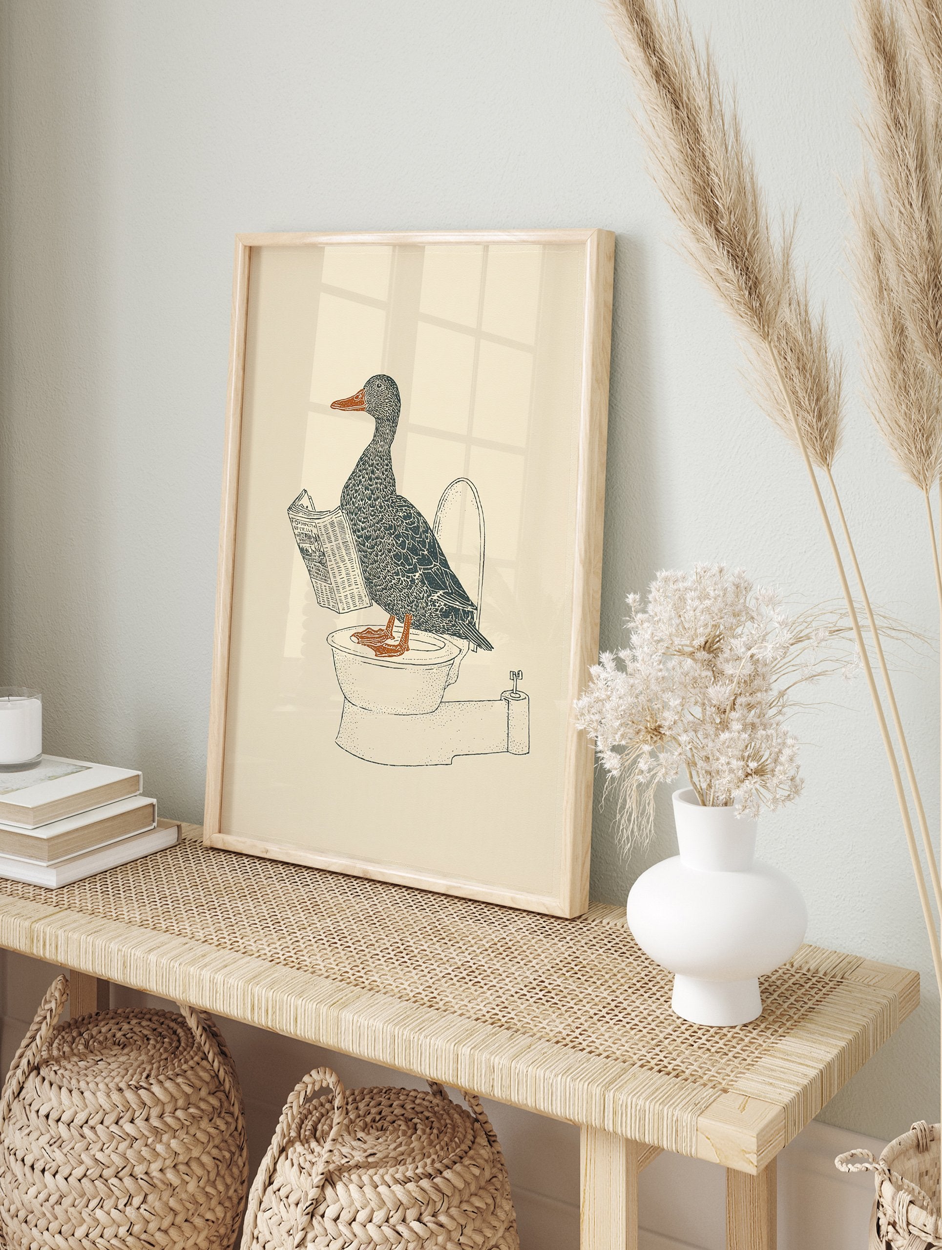 Duck wall art illustration of a gray duck with an orange beak and feet reading a newspaper while sitting on a toilet. - Image 3