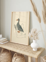 Duck wall art illustration of a gray duck with an orange beak and feet reading a newspaper while sitting on a toilet. - Image 3
