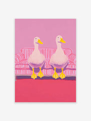 Two white ducks with yellow beaks and feet sitting on a pink and white striped couch in pink room. Duck wall art.