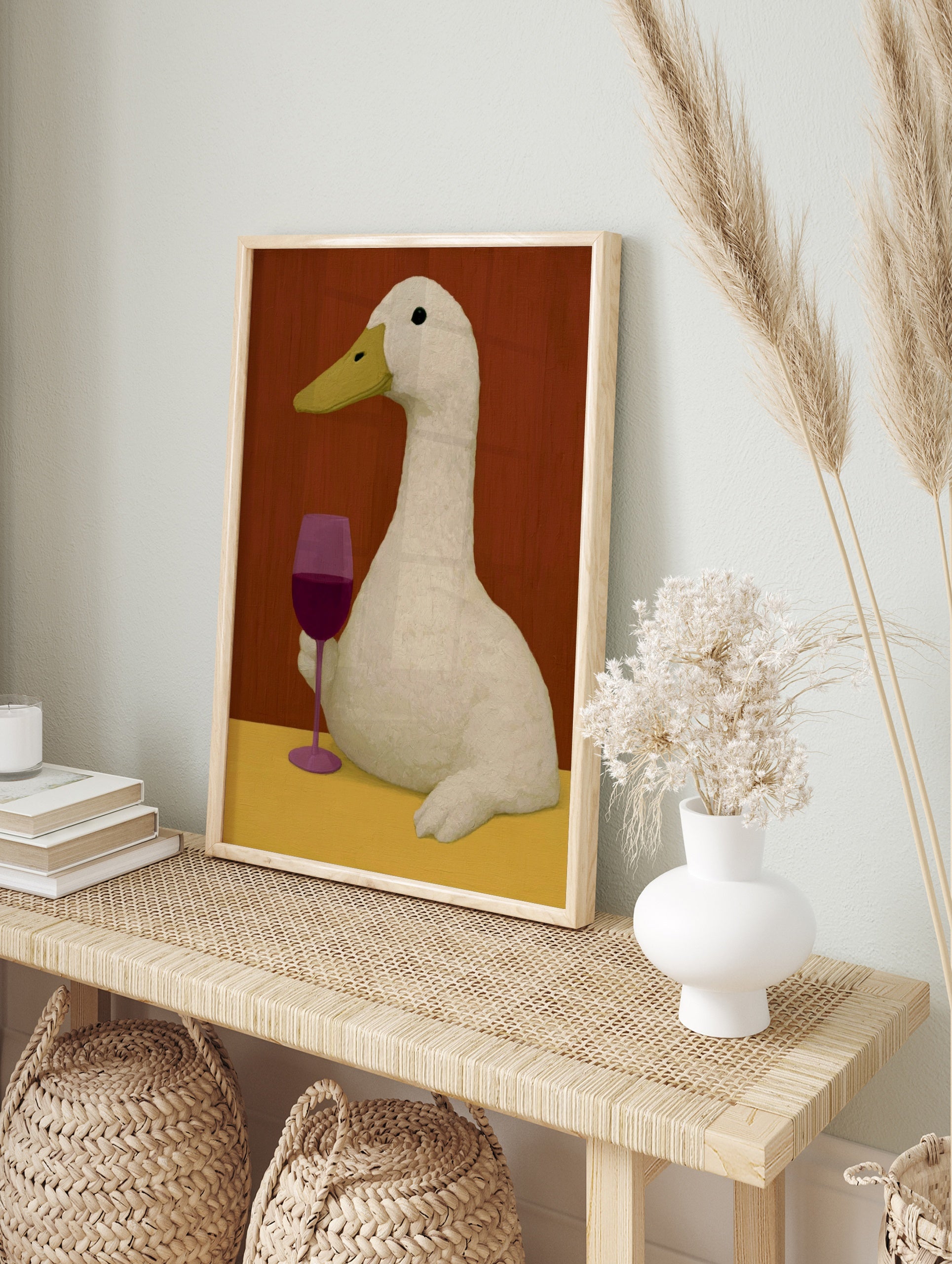 An illustrative art print of a white duck holding a glass of red wine against a warm red, in an alternate framed mockup
