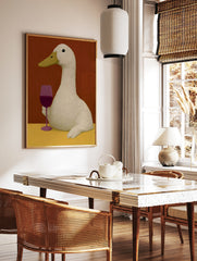 An illustrative art print of a white duck holding a glass of red wine against a warm red background, in a styled room mockup