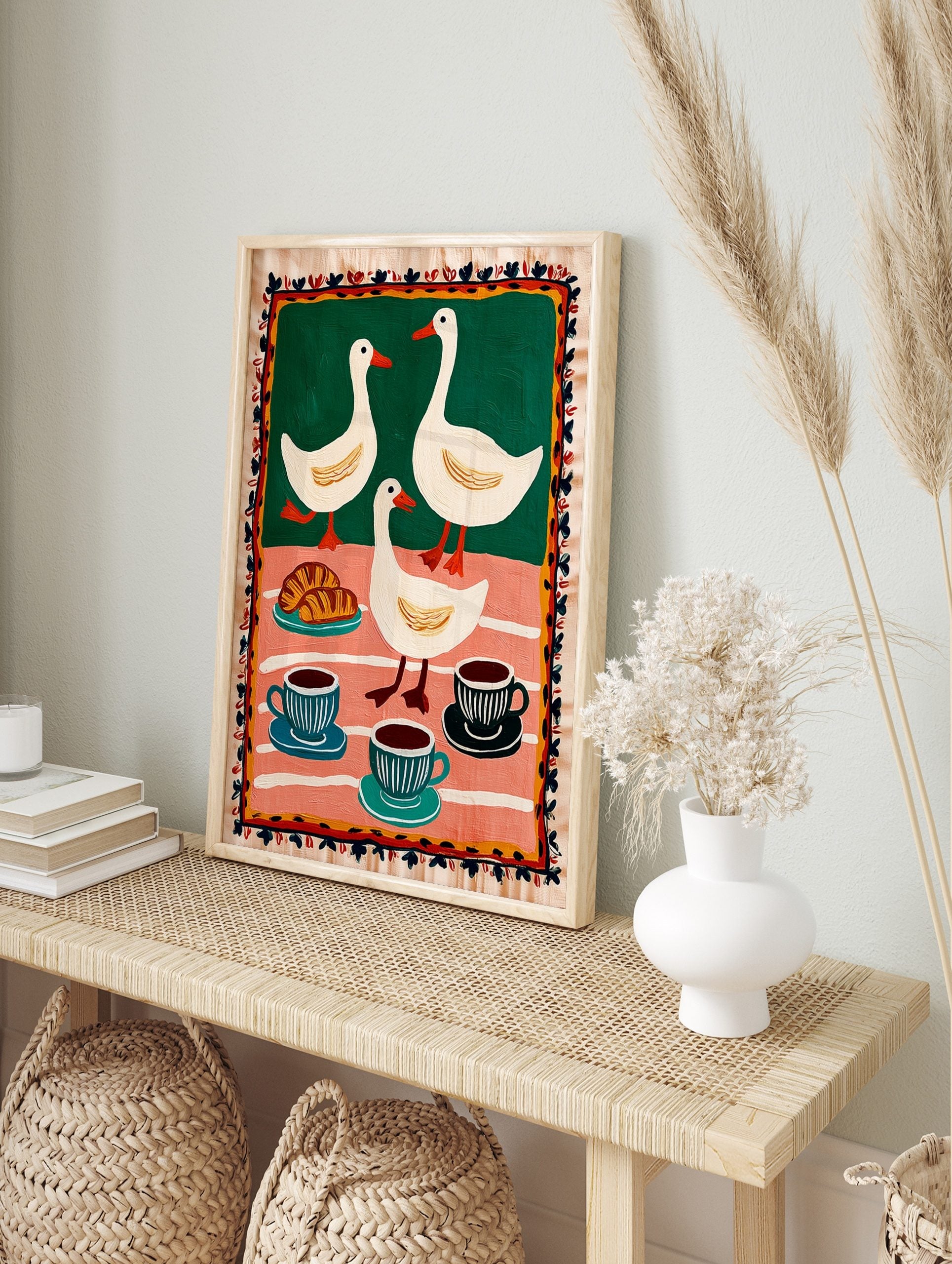 Folk art print of three white ducks, croissants, and coffee cups on green and pink striped, in an alternate framed mockup