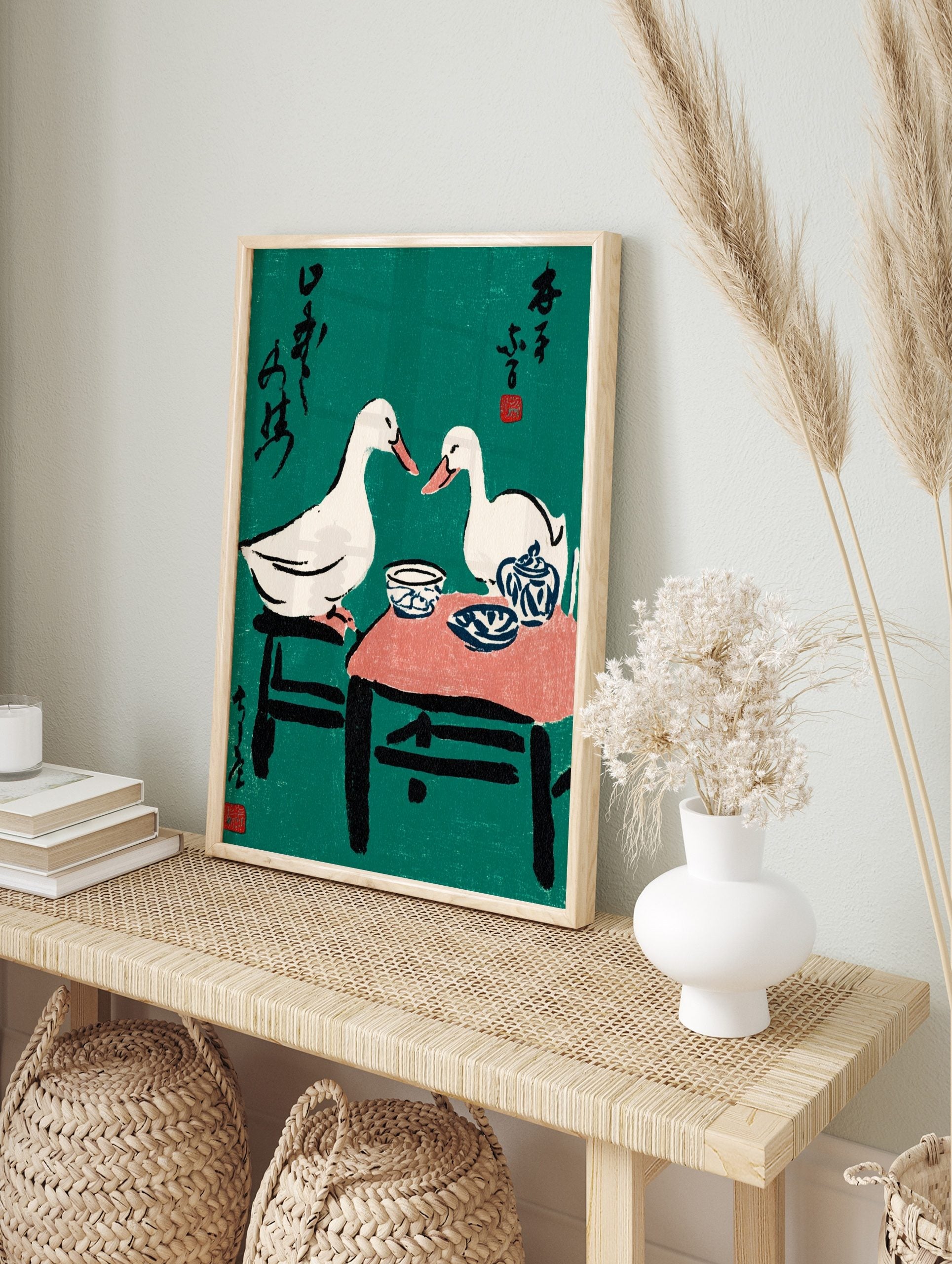 Illustrative print of two white ducks at a tea party with blue pottery, black text, and red, in an alternate framed mockup