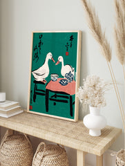 Illustrative print of two white ducks at a tea party with blue pottery, black text, and red, in an alternate framed mockup