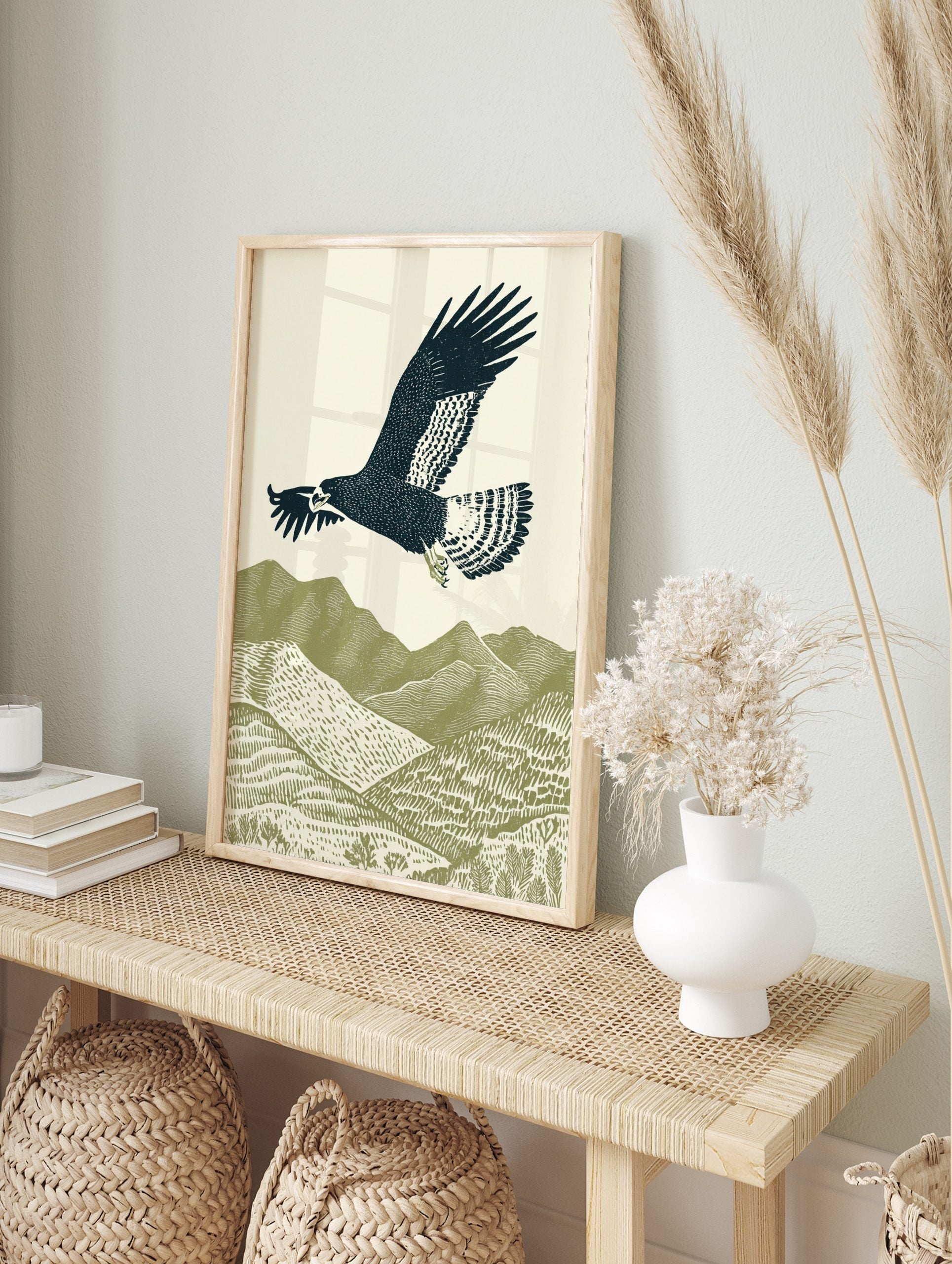 Illustrative woodcut-style print of a dark blue eagle flying over green textured mountains, in an alternate framed mockup