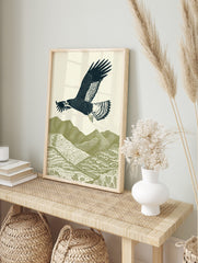 Illustrative woodcut-style print of a dark blue eagle flying over green textured mountains, in an alternate framed mockup