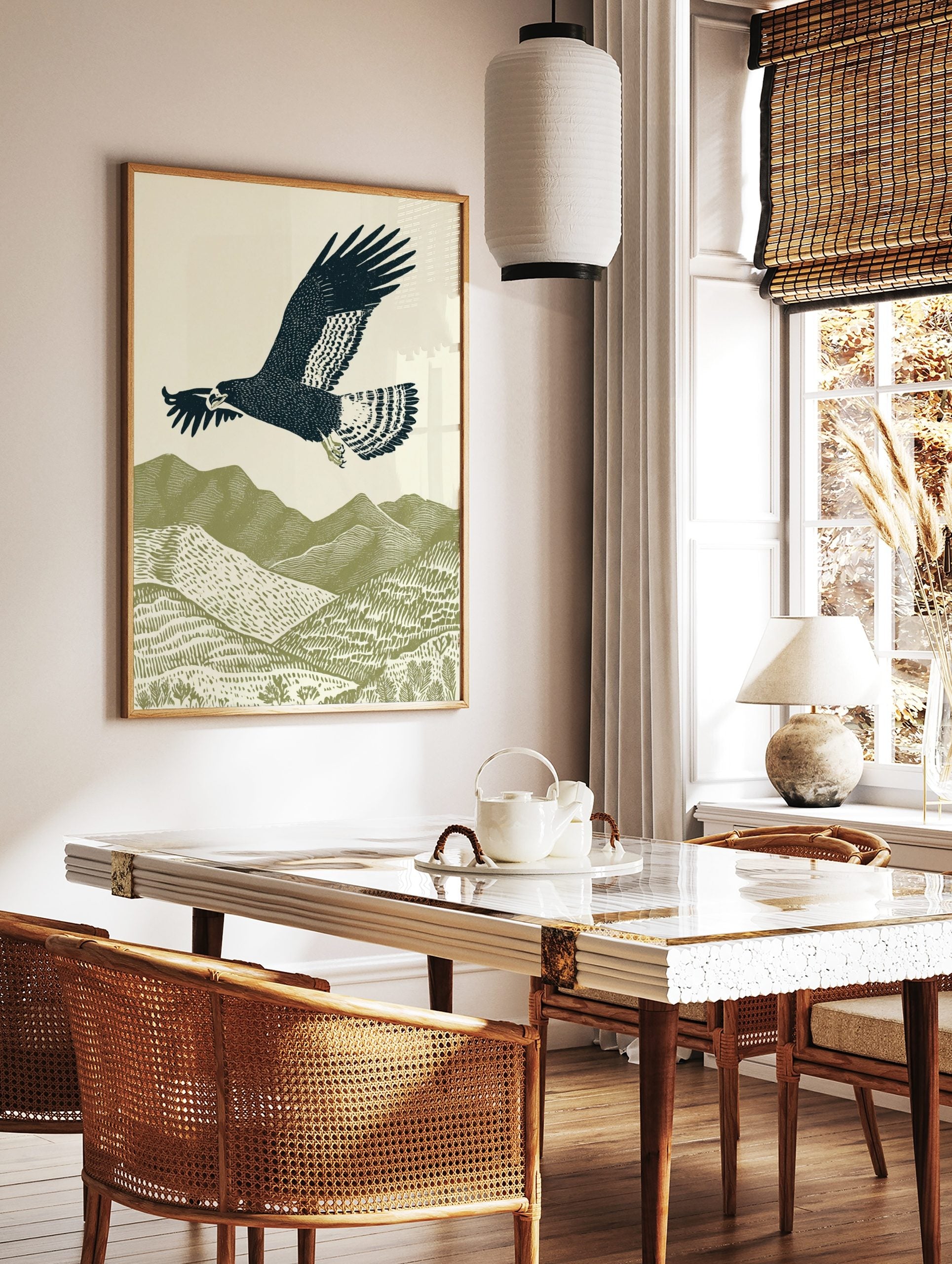 Illustrative woodcut-style print of a dark blue eagle flying over green textured mountains and hills, in a styled room mockup