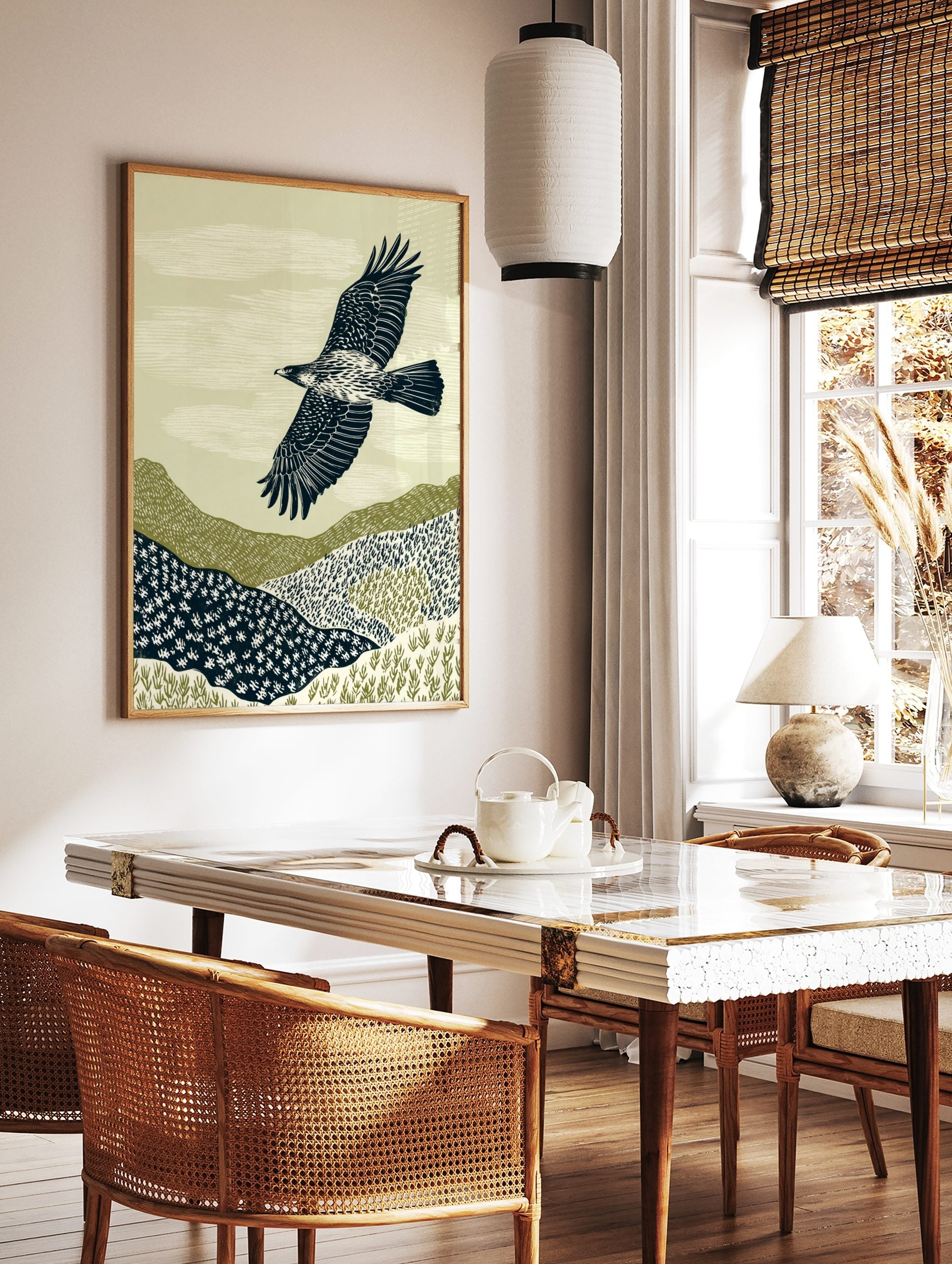 Illustrative print of an eagle with outstretched wings flying over textured green and navy hills, in a styled room mockup