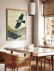 Illustrative print of an eagle with outstretched wings flying over textured green and navy hills, in a styled room mockup
