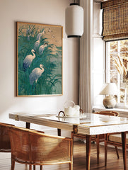 White egrets wading and flying in tall teal marsh grass with a muted sky and water background, in a styled room mockup