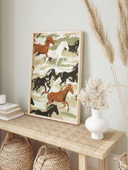 Illustrative print of galloping brown, black, and white horses on a green and beige, in an alternate framed mockup