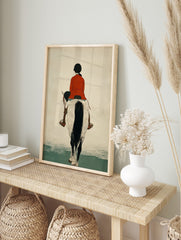 Illustrative print of a horse rider in a red jacket on a white and black horse, viewed from, in an alternate framed mockup