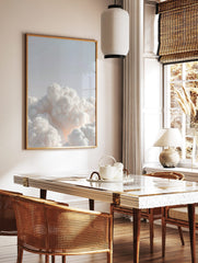 Ethereal white voluminous clouds against a pale blue sky with a soft warm glow, minimalist, in a styled room mockup