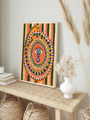Evil eye wall art with blue and yellow concentric dots on a striped background, illustrative, in an alternate framed mockup