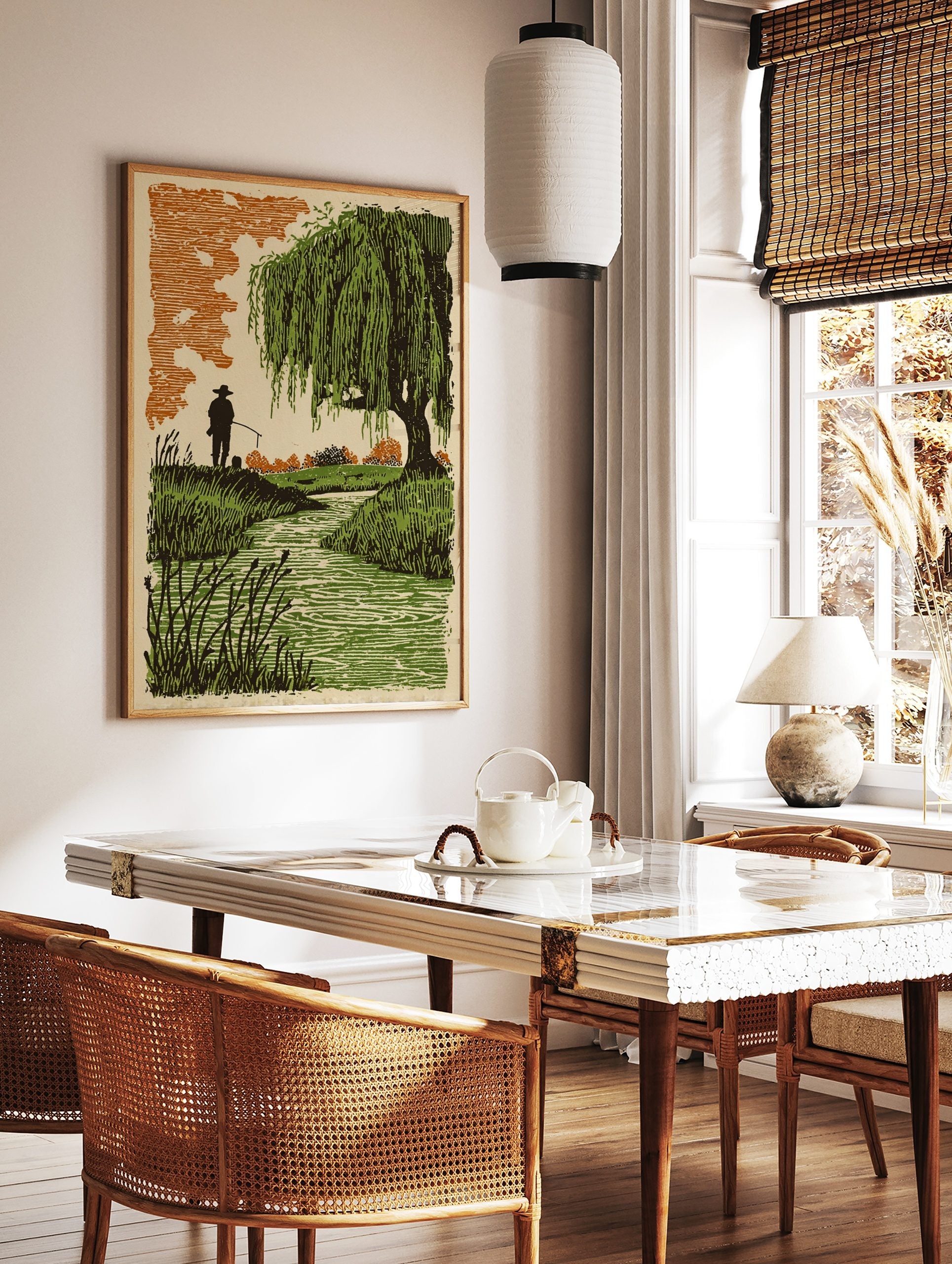 Woodcut style print of a fisherman by a stream with a large weeping willow tree and orange sky, in a styled room mockup