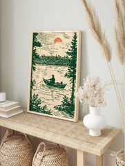 Illustrative print of a fisherman in a boat on a lake, framed by pine trees, under a setting, in an alternate framed mockup