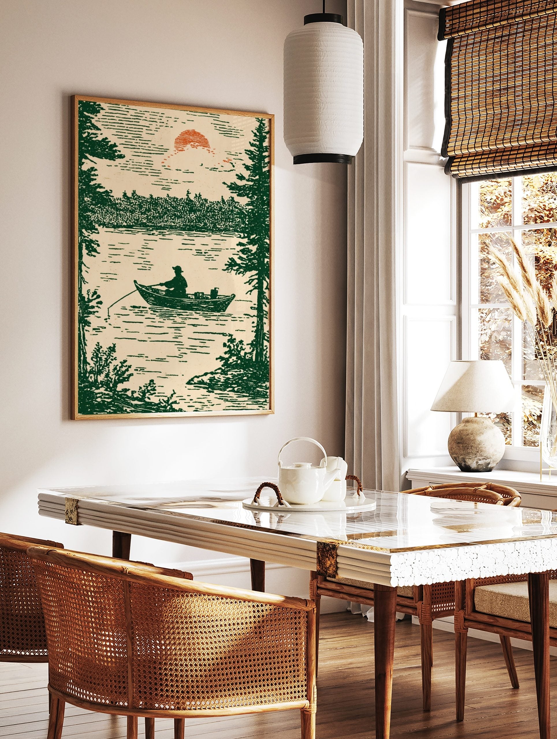 Illustrative print of a fisherman in a boat on a lake, framed by pine trees, under a setting sun, in a styled room mockup
