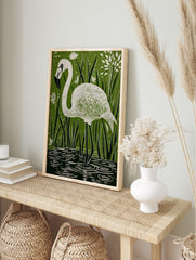 White flamingo in linocut style, standing in water among green reeds and white flowers, in an alternate framed mockup