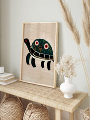 Illustrative dark green turtle wall art print with floral decorated shell and red eyes on, in an alternate framed mockup