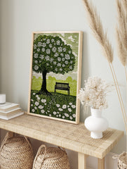 Linocut style print of a flowering tree, park bench, and wildflowers in a green field with, in an alternate framed mockup