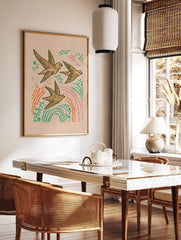 Illustrative print of three flying swallows with green leaves, orange plants, and pink streaks on, in a styled room mockup