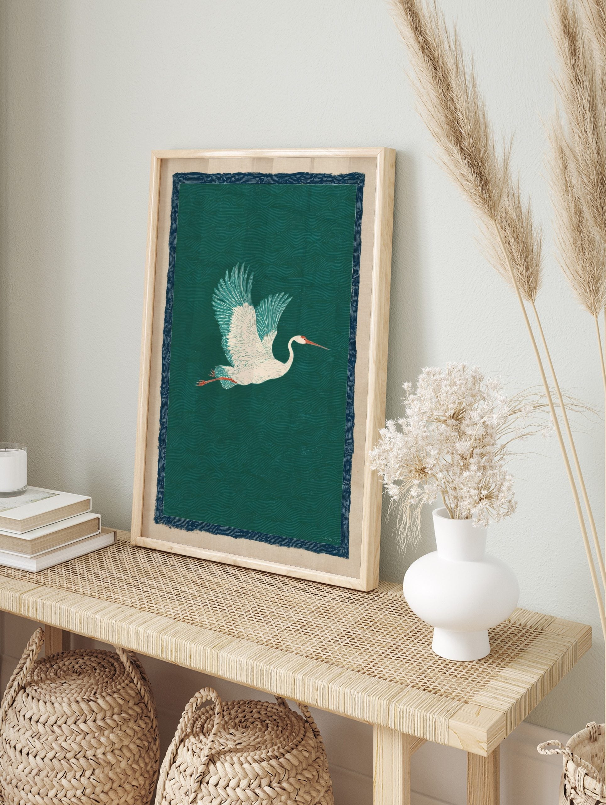 White crane bird with teal wings flying against a deep green wave-patterned background, with, in an alternate framed mockup