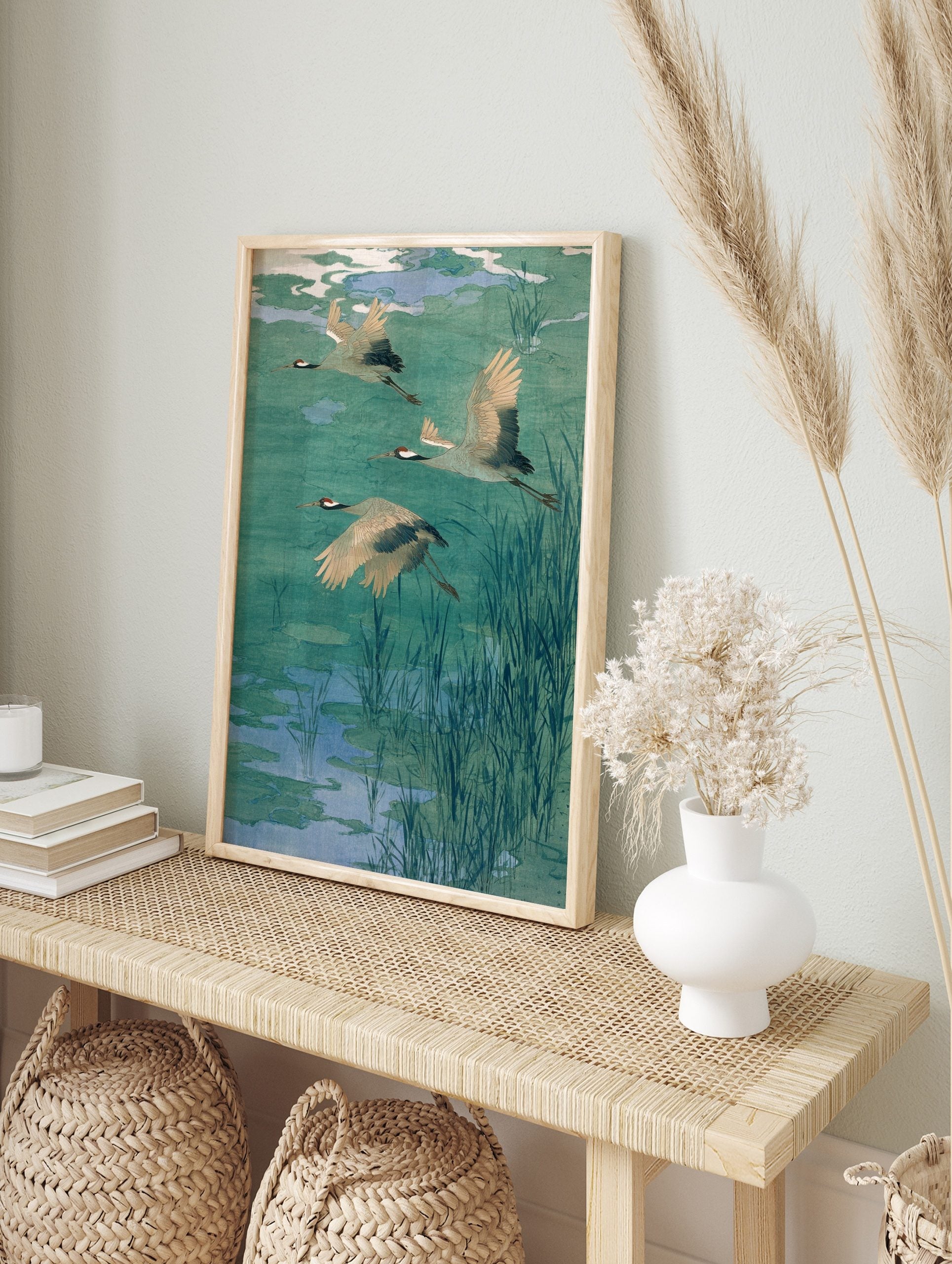 Three flying cranes with red heads and black wing tips over a teal and blue pond with reeds, in an alternate framed mockup