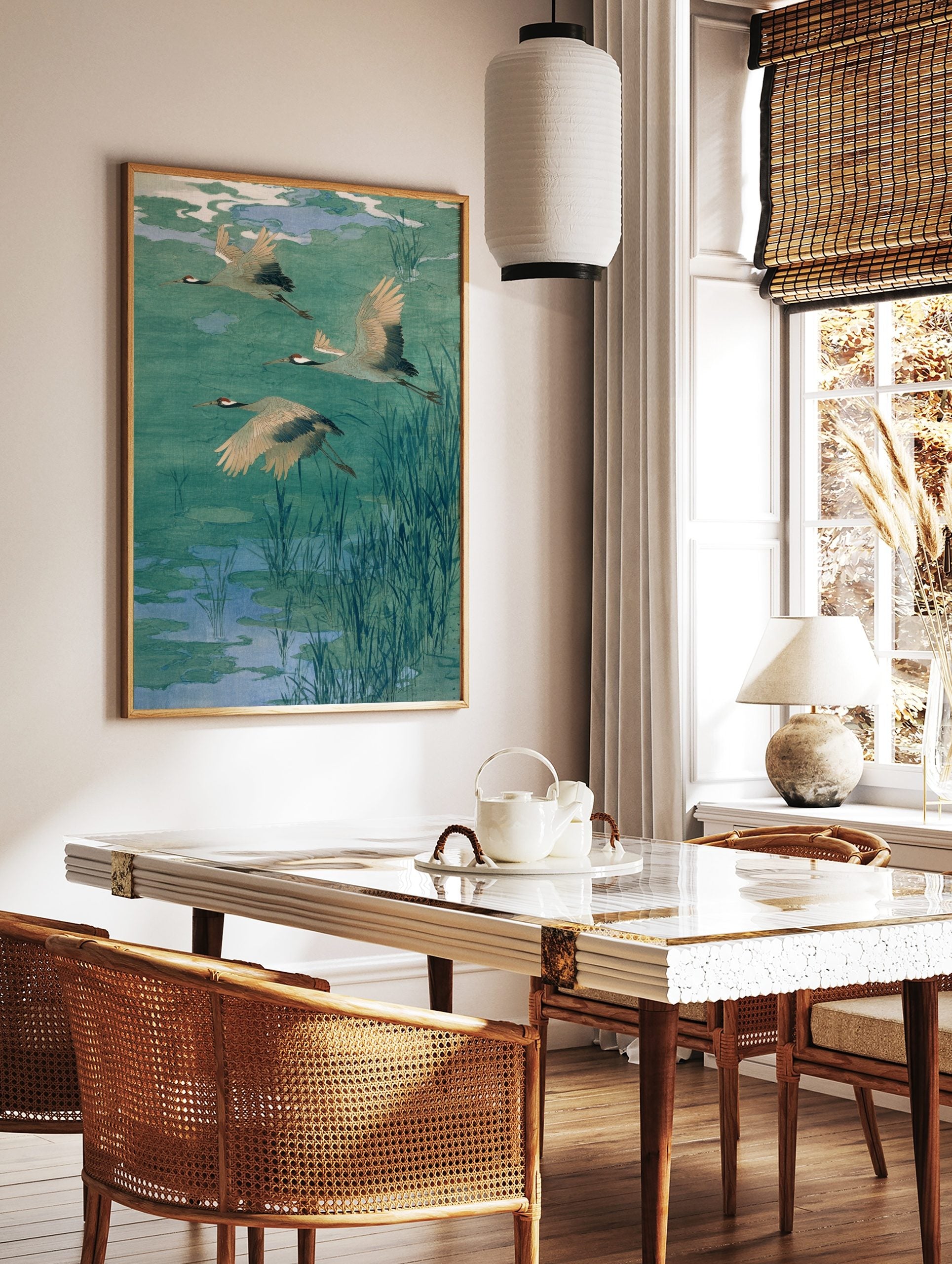 Three flying cranes with red heads and black wing tips over a teal and blue pond with reeds, in a styled room mockup