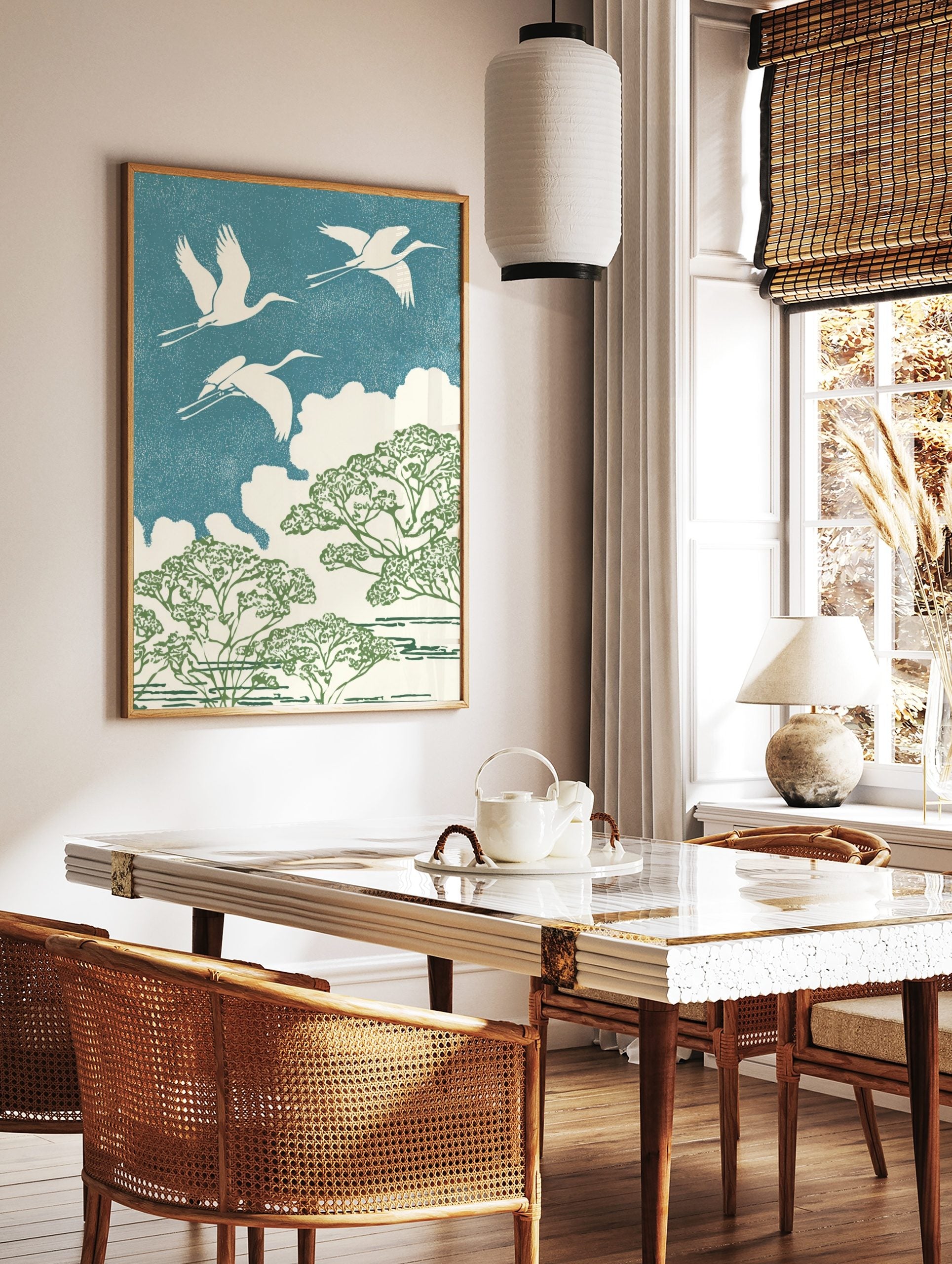 Three white cranes flying over green trees and white clouds against a textured blue sky in an, in a styled room mockup