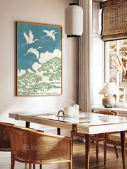 Three white cranes flying over green trees and white clouds against a textured blue sky in an, in a styled room mockup