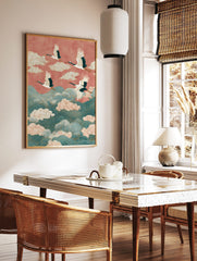 Four white cranes with red crowns fly over teal waves and pink clouds against a coral sky in an, in a styled room mockup